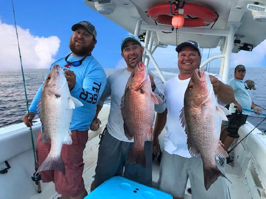 Three men on a boat holding large snapper fish caught with saltwater jigs