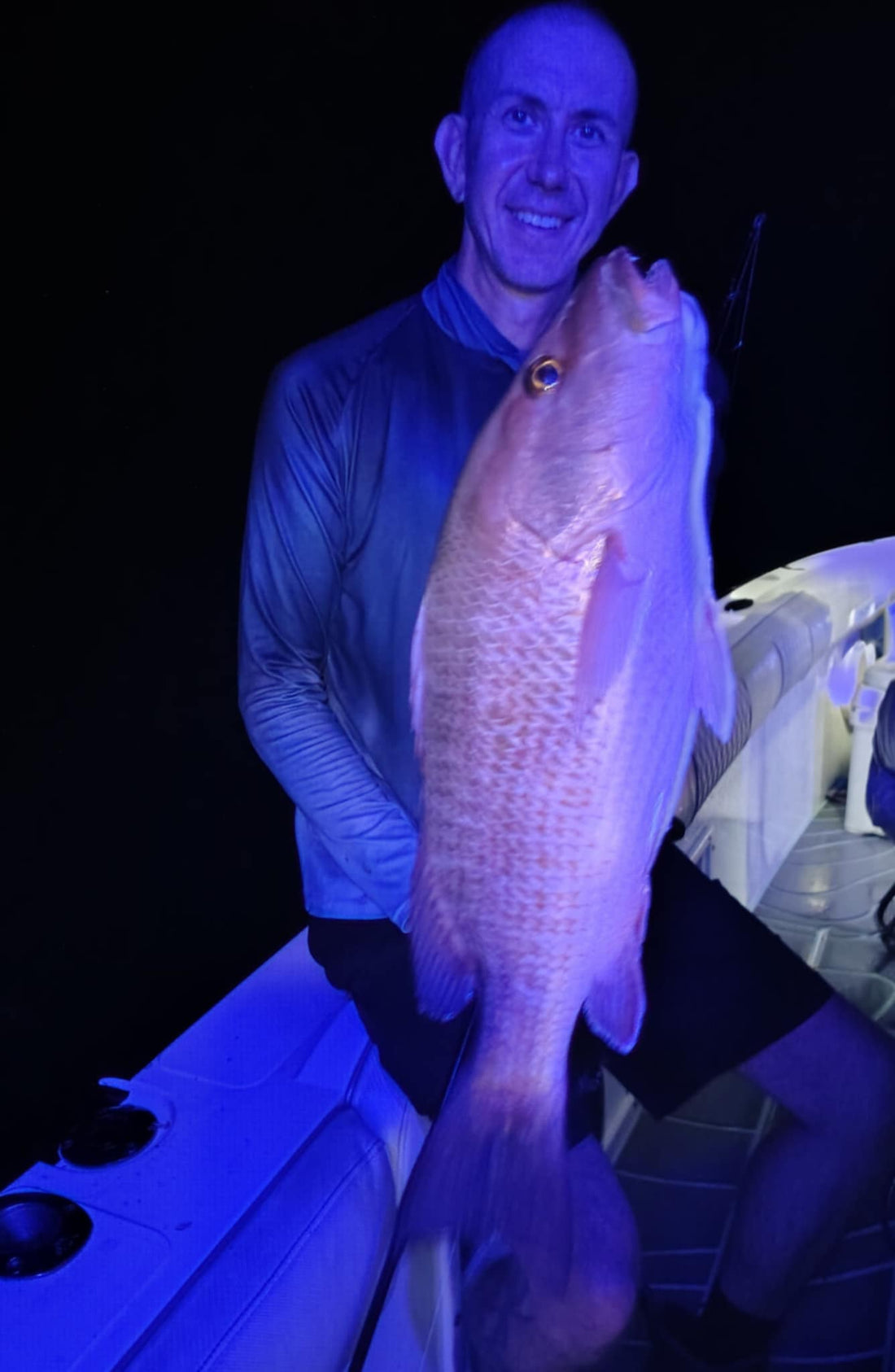 Angler holding large snapper caught with saltwater fishing jig on boat at night