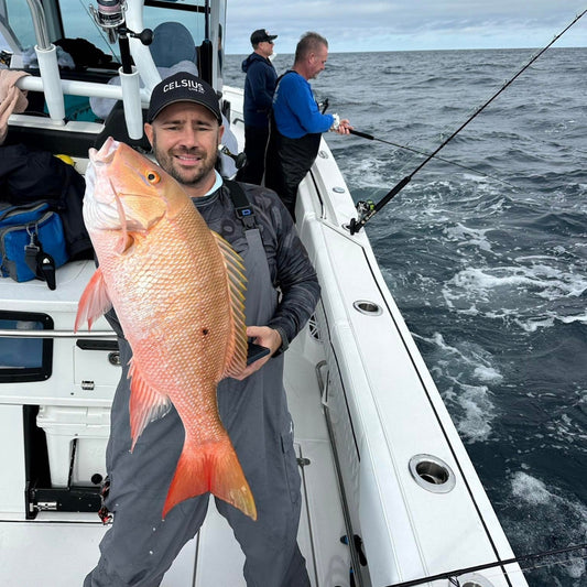 Angler holding large snapper caught offshore, showcasing successful saltwater fishing jig results on a boat