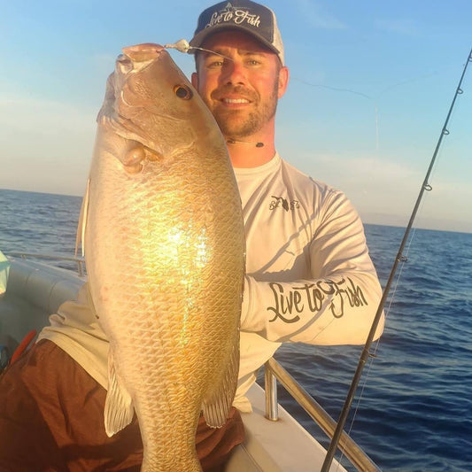 Angler holding large snapper caught with offshore fishing jig on boat at sunset